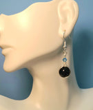 Image of an of earring with round Blue Sandstone bead wrapped with silver wire and topped with blue Swarovski crystals hanging from a mannequin 