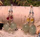 Image of two pairs of Green Aventurine earrings wrapped by silver wire topped by a daisy bead and red Swarovski crystals or yellow Swarovski crystals hanging from birch bark over pine branches and an artificial snowflake