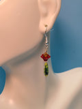 Red 5 point flowers topped by yellow Swar. crystals over green dagger beads dangling from sterling silver hooks in the ear of a manequin.