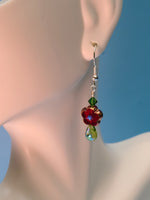 Picture of Red sparkly flower with a green crystal above and shiny glass drop below. Dangling from gold toned sterling silver hook on a mannequins ear. 