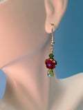 Picture of Red sparkly flower with a green crystal above and shiny glass drop below. Dangling from gold toned sterling silver hook on a mannequins ear. 