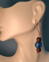 Image of an earring with blue colored recycled glass from Ghana with blood sandalwood beads over and under the glass bead on copper wire hanging on a mannequin