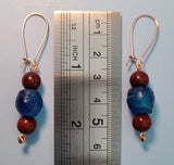 Image of a pair of earrings with blue colored recycled glass from Ghana with blood sandalwood beads over and under the glass bead on copper wire next to a ruler measuring 2 1/4"