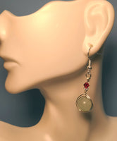 Image of a Green Aventurine earring wrapped by silver wire topped by a daisy bead and red Swarovski crystal hanging from a mannequin