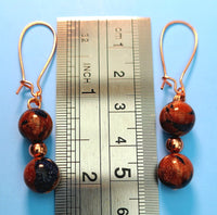 Image of earrings of Bicolored Sandstone beads separated by a copper bead pictured with a ruler measuring 2 1/4 inches