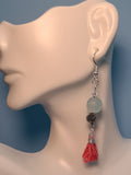 Image of an earring with aqua colored recycled glass bead from Ghana a tree of life bead and pink tassel hung on silver wire on a mannequin