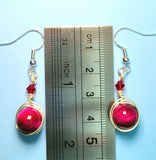 Image of 1 pair of earrings with pink tiger eye 10mm beads wrapped by silver wire and topped by a red 4mm Swarovski crystal by a ruler measuring 1 3/4"