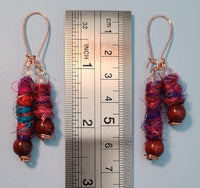 Image of earrings made of Silk Sari Yarn, round Sandalwood beads, crystal beads and copper wire against a ruler 2 1/2 inches long